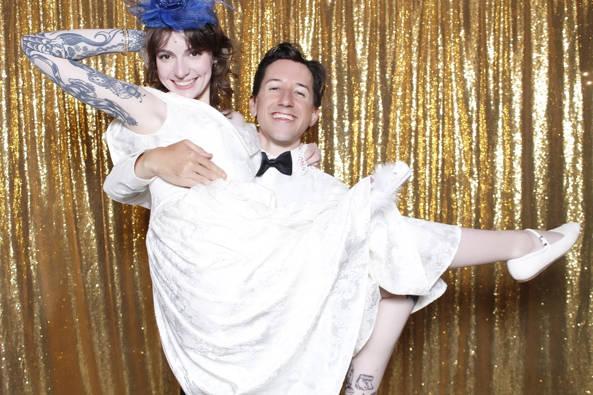 Alyssa and Derek laughing as Derek holds Alyssa in front of a gold sequin backdrop