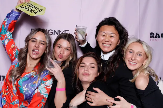 Five guests posing together in front of a branded event backdrop.
