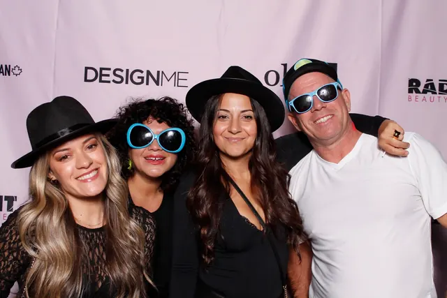 Four guests wearing hats and sunglasses in front of a branded step-and-repeat backdrop.
