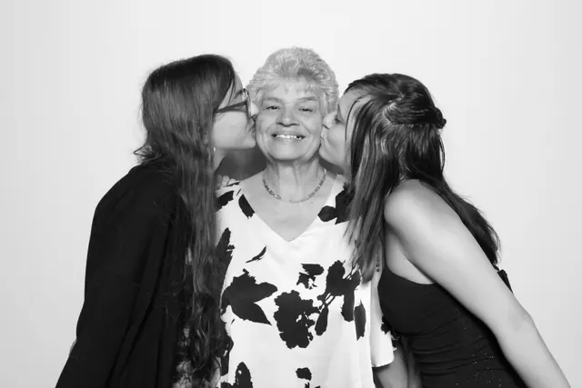 Two guests kissing a smiling older guest on the cheeks in a black-and-white portrait.
