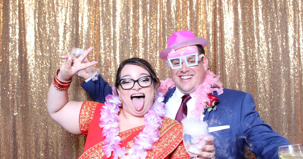 Couple celebrating with photo booth props in front of a gold sequin backdrop