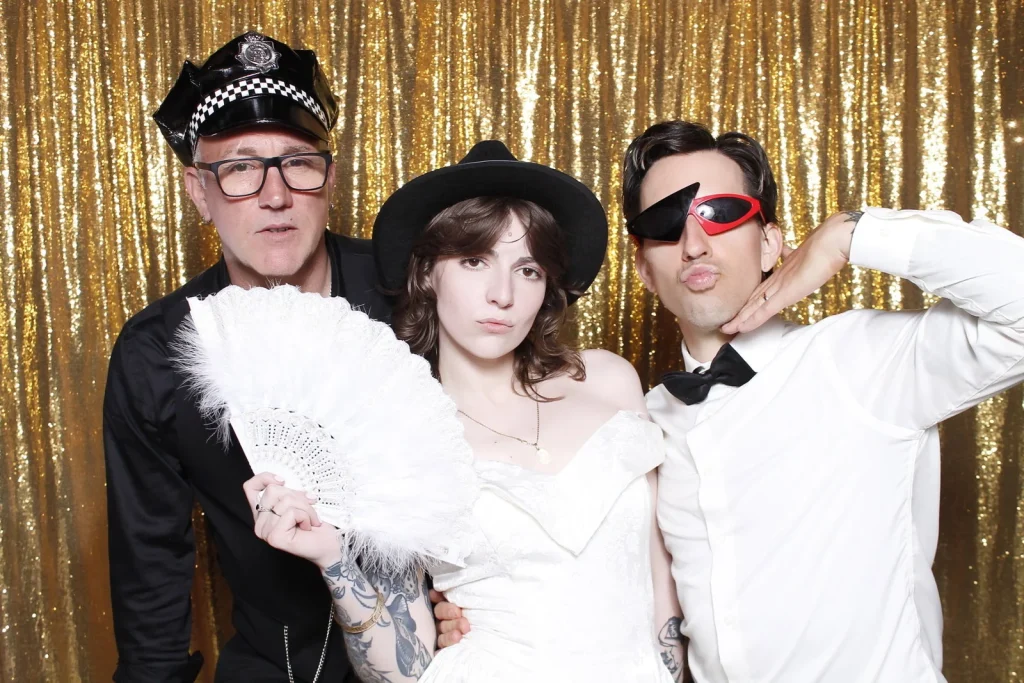 Three wedding guests posing with hats, novelty glasses, and a feather fan