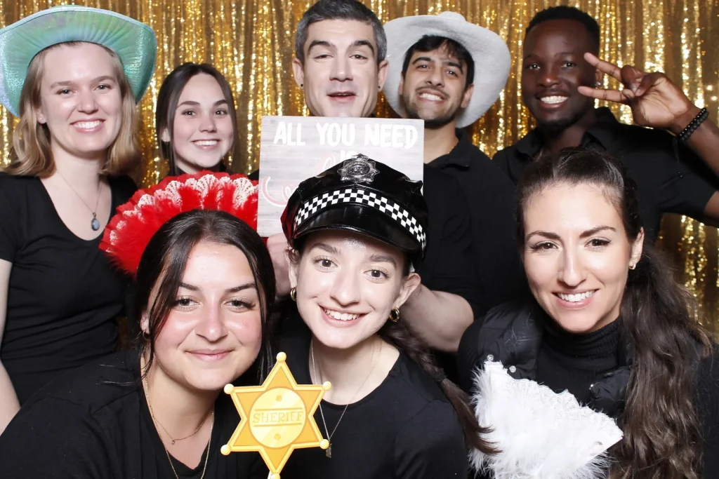 A group of wedding guests crowding into the frame with playful photo booth props