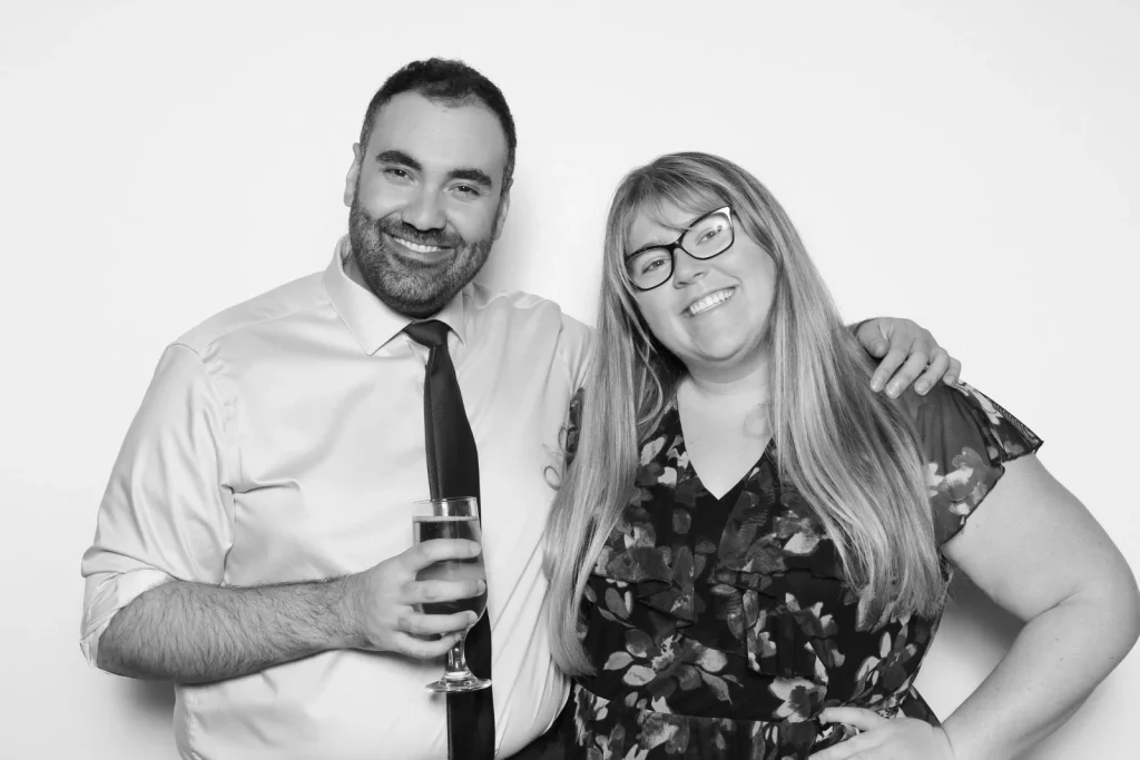 Two wedding guests smiling together against a clean white background in black and white